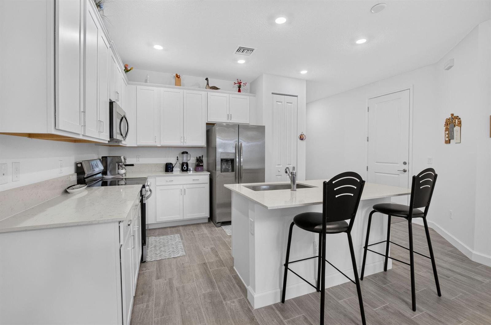 A modern kitchen features white cabinets, stainless steel appliances, a quartz island, and tile flooring — 13828 Hero Path, Delray Beach FL 33484, DELRAY BEACH, FL