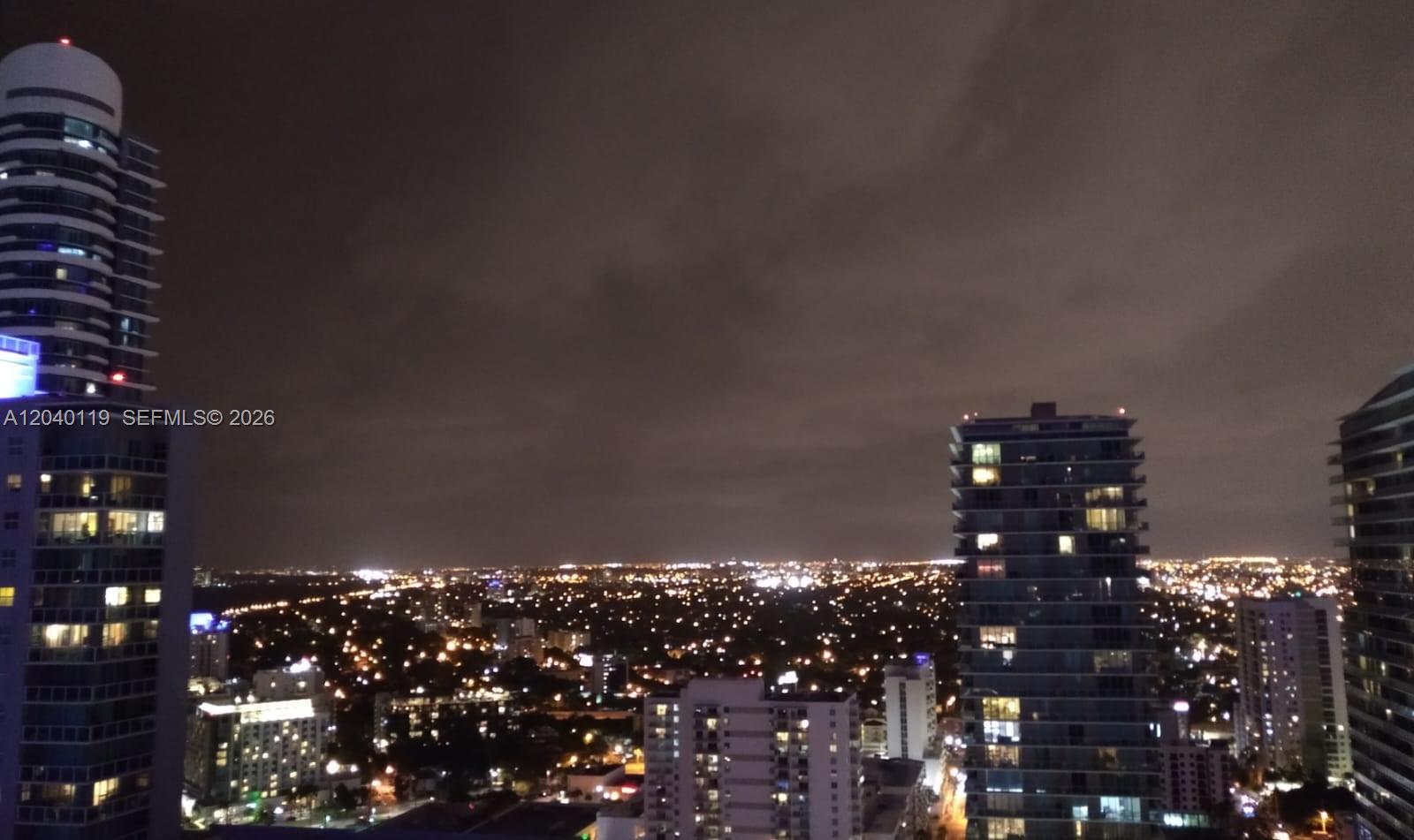 A high-angle night view of a city skyline featuring several illuminated residential high-rise buildings — 1080 Brickell Ave # 3203, Miami FL 33131, MIAMI, FL