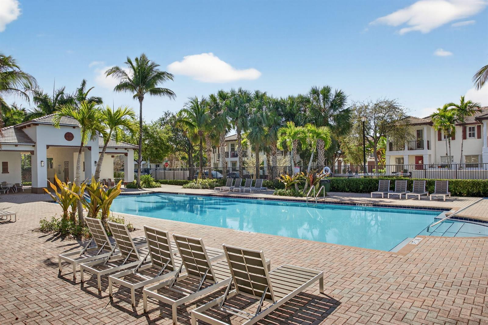 A swimming pool surrounded by lounge chairs, palm trees, and apartment buildings under a blue sky — 4718 Monarch Way, Coconut Creek FL 33073, COCONUT CREEK, FL