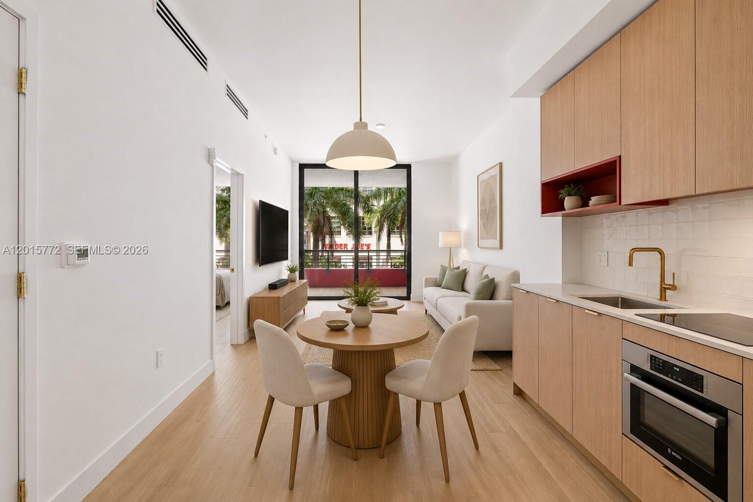 A modern apartment living area features a kitchen, dining table, and balcony with palm trees — 90 NE 32nd St # 211, Miami FL 33127, MIAMI, FL