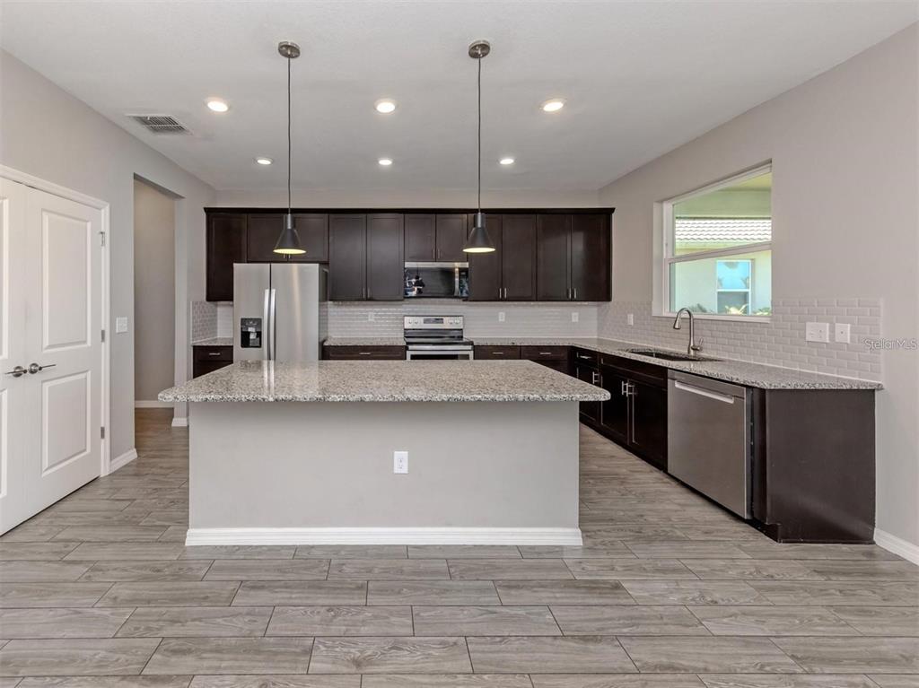 A kitchen features dark wood cabinets, granite countertops, stainless steel appliances, and gray wood-look flooring — 2160 WEAVER BIRD LANE, VENICE, FL