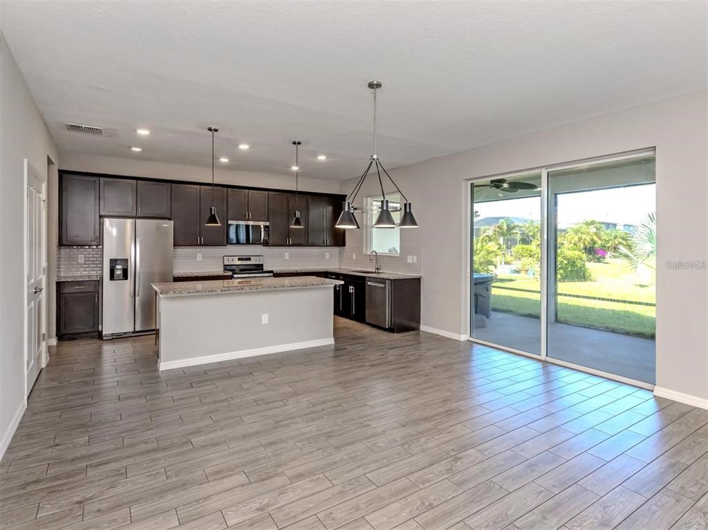 A kitchen with dark cabinets, granite countertops, and tile flooring opens to a sliding glass door — 2160 WEAVER BIRD LANE, VENICE, FL