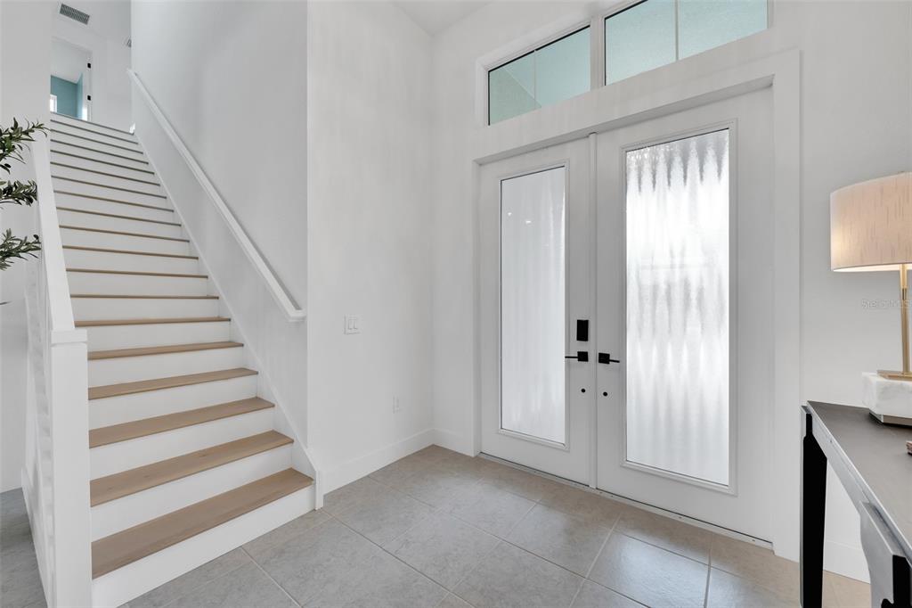 A bright entryway features a white staircase with wood treads and a double glass front door — 8444 CANE BAY COURT, LAKEWOOD RANCH, FL