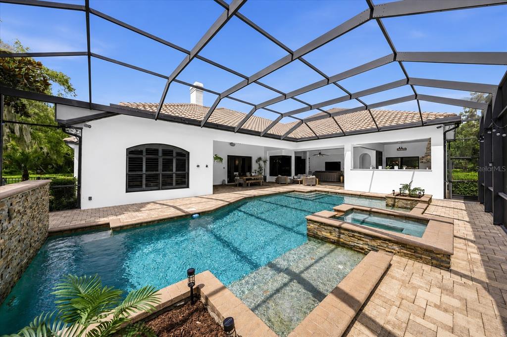 A screened-in patio features a swimming pool with a hot tub and stone accents — 16303 DUNLINDALE DRIVE, LITHIA, FL