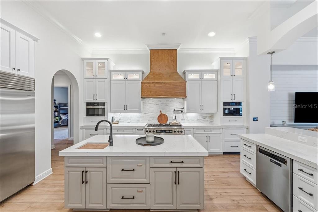 A modern kitchen features white cabinetry, a wood range hood, and a central island — 16303 DUNLINDALE DRIVE, LITHIA, FL