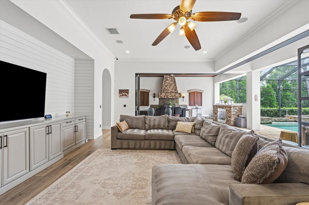 A living room features a large sectional sofa, built-in cabinetry, and a view of a pool — 16303 DUNLINDALE DRIVE, LITHIA, FL