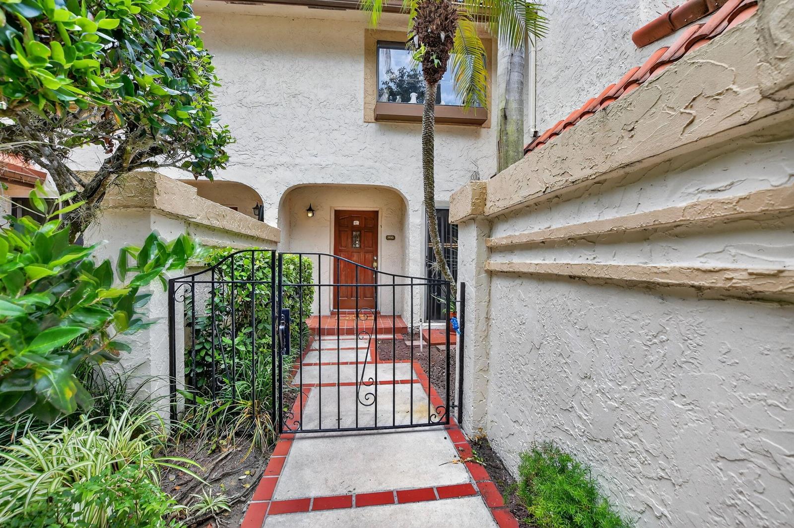 A gated walkway leads to the front entrance of a stucco home with a wooden door — 7773 La Mirada Drive, Boca Raton FL 33433, BOCA RATON, FL