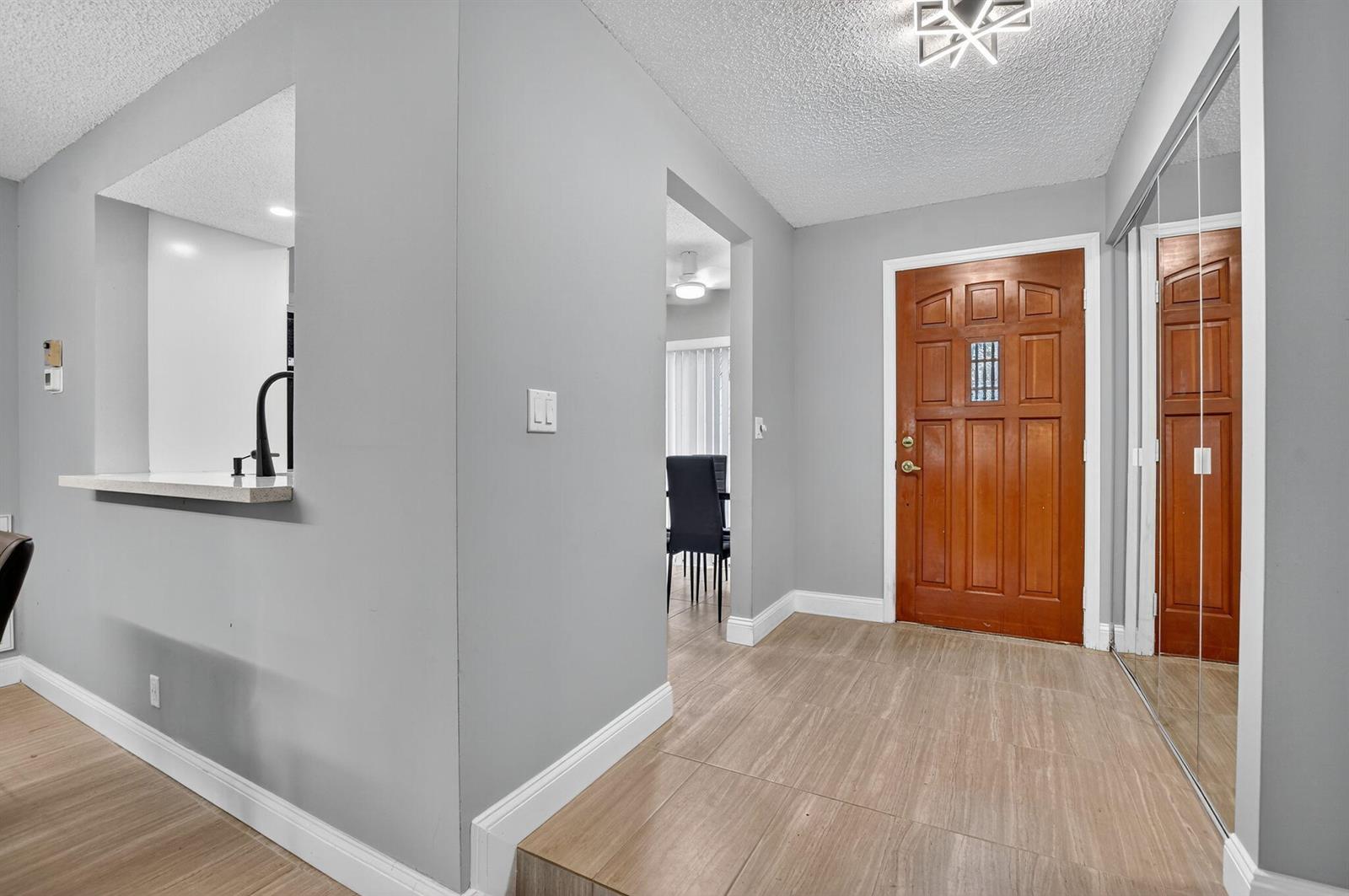 An entryway features light wood-look flooring, gray walls, a wooden front door, and mirrored closets — 7773 La Mirada Drive, Boca Raton FL 33433, BOCA RATON, FL