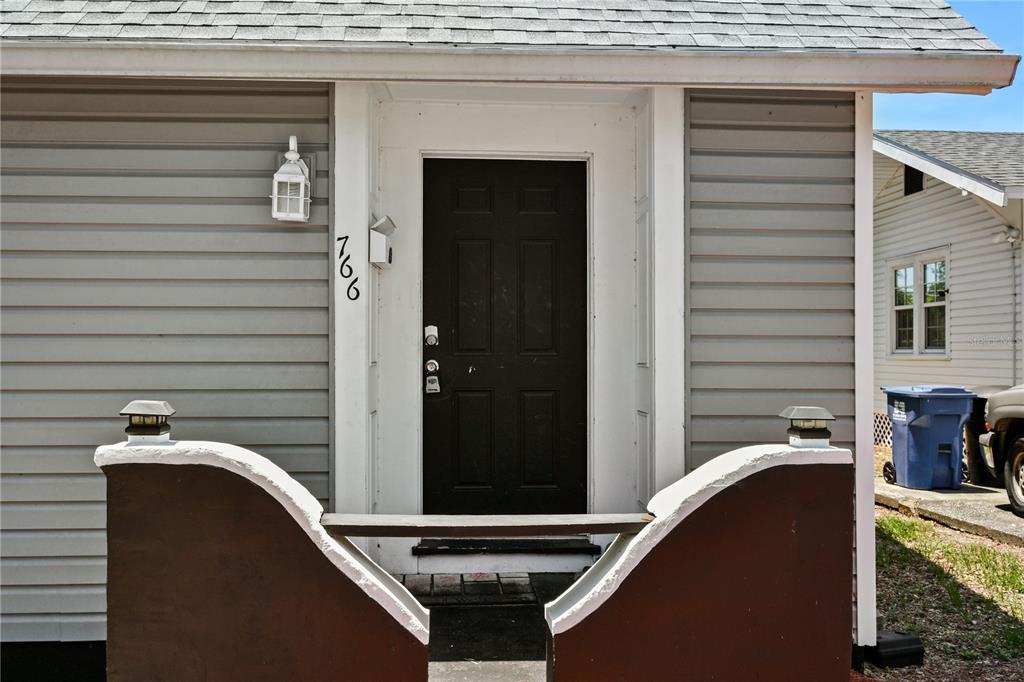A dark front door with the house number 766 is centered on a gray-sided house — 766 13TH AVENUE S, ST PETERSBURG, FL