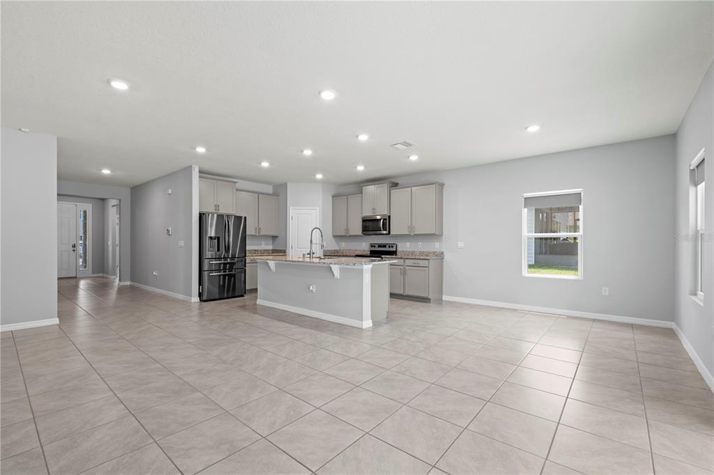 An open-concept kitchen features gray cabinets, granite countertops, a center island, and tiled flooring — 17387 NW 172ND AVENUE, ALACHUA, FL