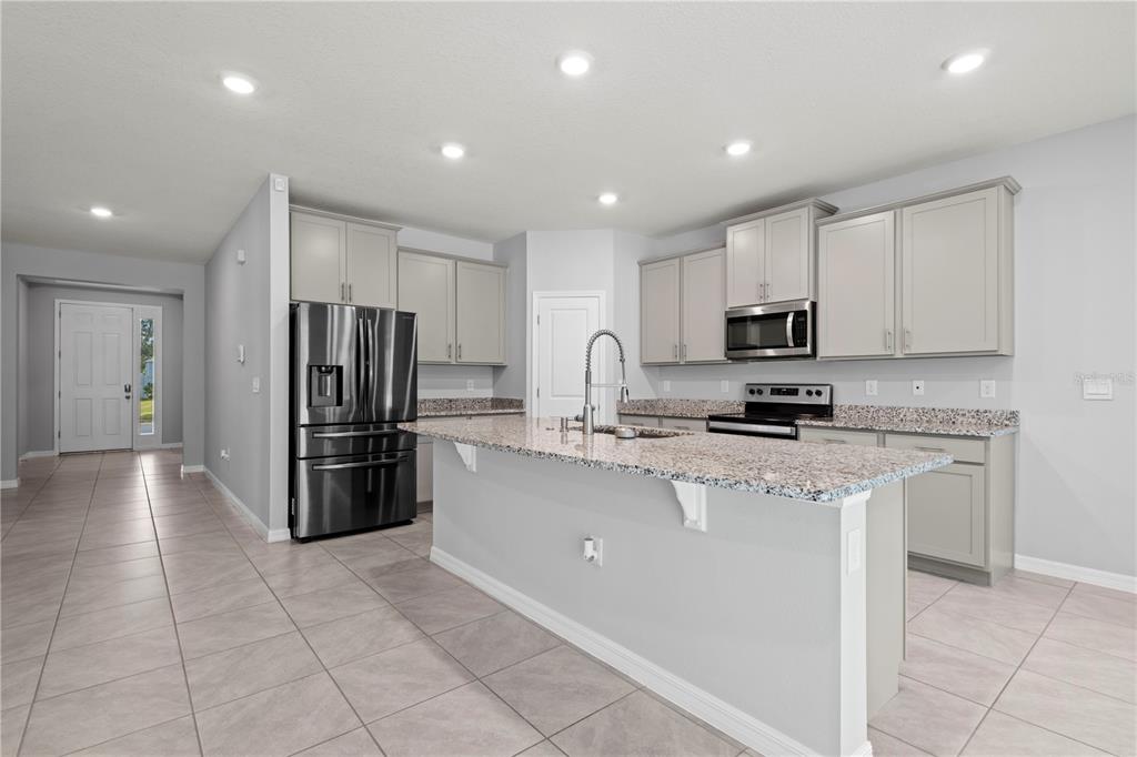 A modern kitchen features light gray cabinets, granite countertops, a center island, and stainless appliances — 17387 NW 172ND AVENUE, ALACHUA, FL