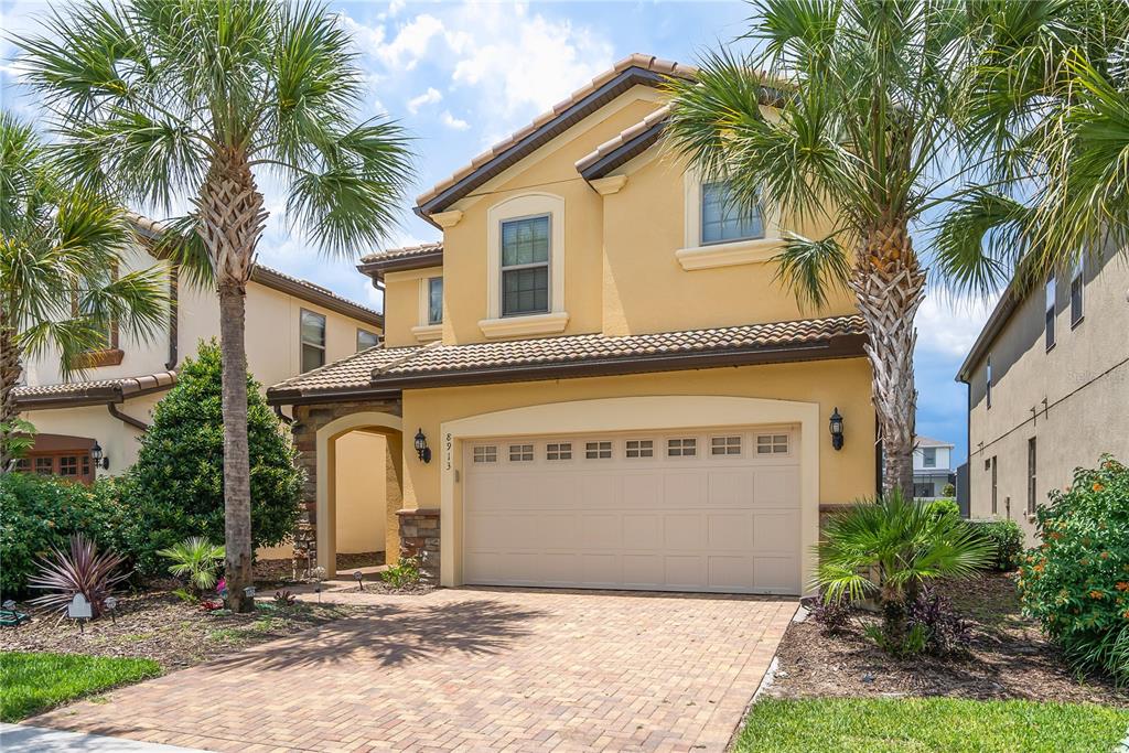 A two-story yellow stucco house features a two-car garage and a brick paver driveway — 8913 RHODES STREET, KISSIMMEE, FL