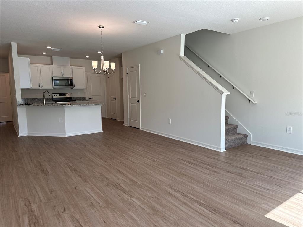 An open-concept living area features wood-look flooring, a kitchen with white cabinets, and a staircase — 9354 WESTSIDE HILLS DRIVE, DAVENPORT, FL