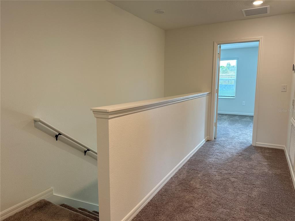 A carpeted hallway features a staircase with a white railing and a doorway to a bedroom — 9354 WESTSIDE HILLS DRIVE, DAVENPORT, FL