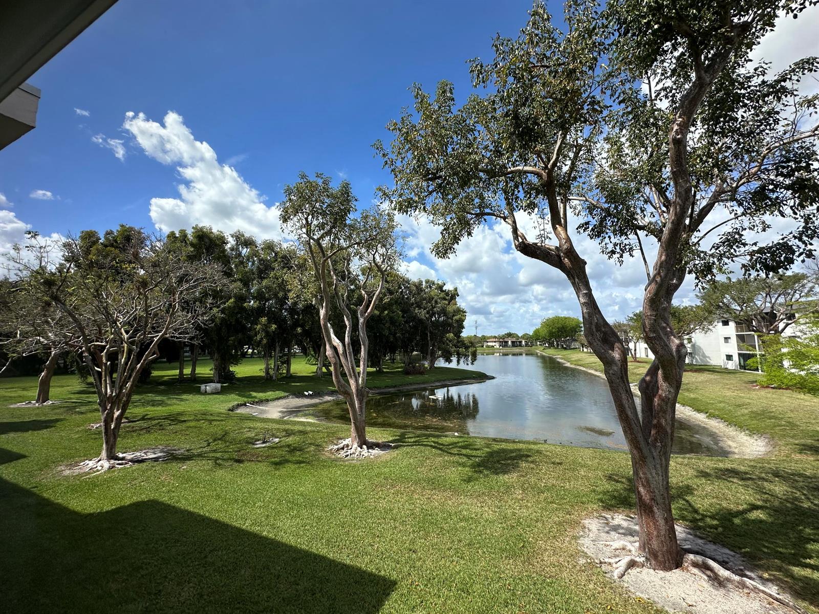A grassy lawn with trees overlooks a small pond near a residential building — 15075 Witney Road # 211, Delray Beach FL 33484, DELRAY BEACH, FL