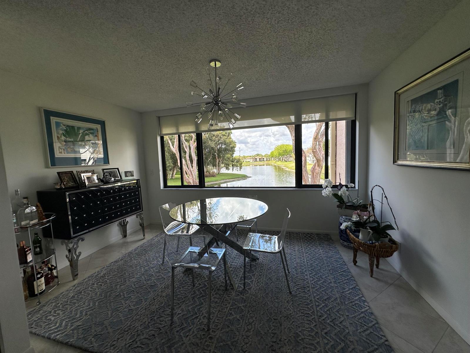 A dining room features a glass table, acrylic chairs, a patterned rug, and a lake view — 15075 Witney Road # 211, Delray Beach FL 33484, DELRAY BEACH, FL