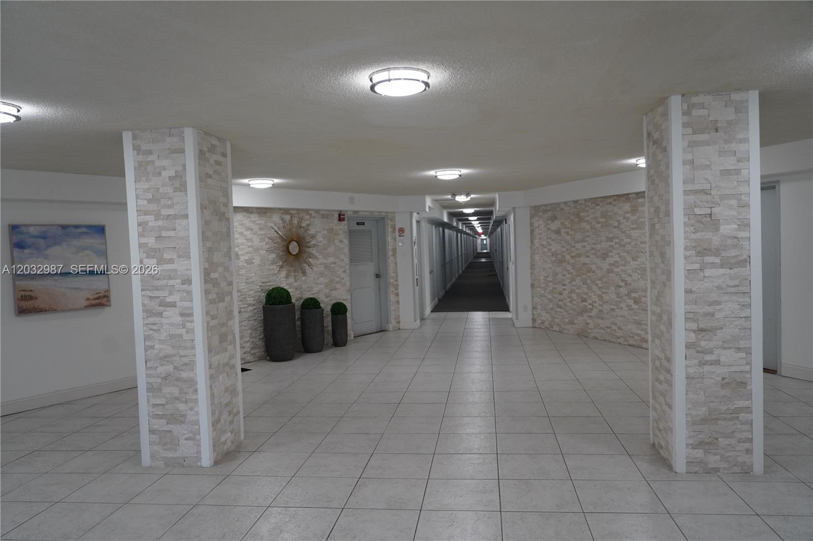 A tiled hallway features stone-clad columns and recessed lighting leading to a long corridor — 1913 S Ocean Dr # 405, Hallandale Beach FL 33009, HALLANDALE BEACH, FL