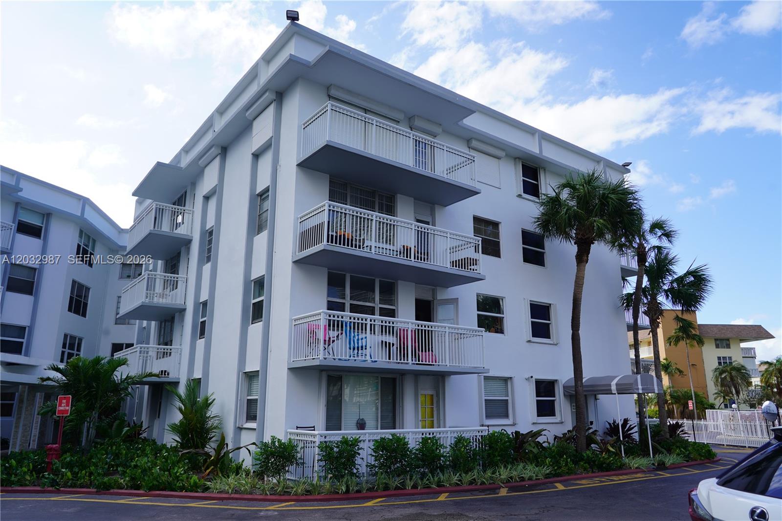 A multi-story white apartment building features stacked balconies and palm trees in the foreground — 1913 S Ocean Dr # 405, Hallandale Beach FL 33009, HALLANDALE BEACH, FL
