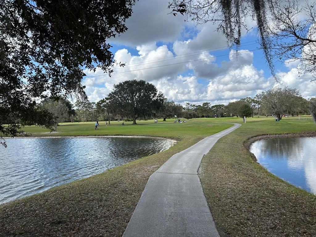 A concrete path leads through a golf course between two ponds under a cloudy sky — 420 HIBISCUS DRIVE, INDIAN LAKE ESTATES, FL
