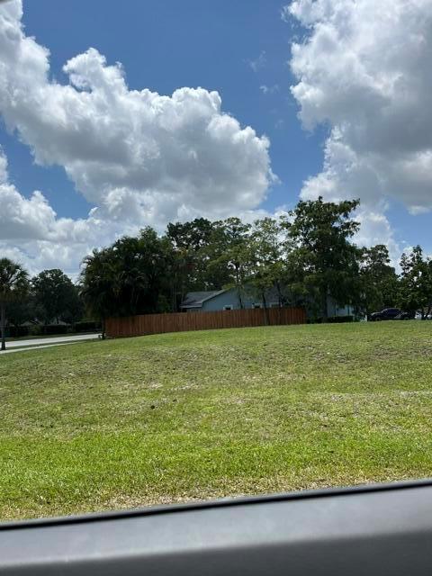 A grassy, sloped vacant lot features a wooden fence and trees in the background — 1094 Primrose Lane, Wellington FL 33414, WELLINGTON, FL