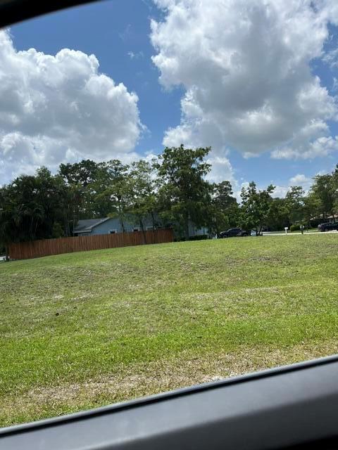 A grassy, slightly sloped vacant lot features a wooden fence and trees in the background — 1094 Primrose Lane, Wellington FL 33414, WELLINGTON, FL