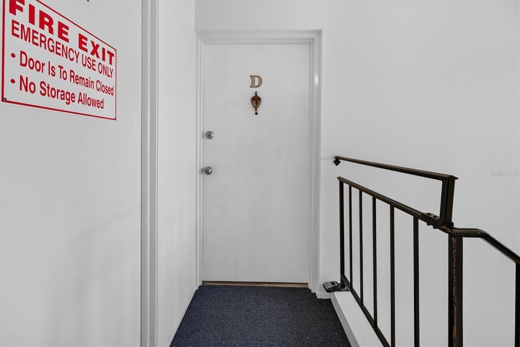 A white door labeled D is situated next to a black metal stair railing — 8522 10TH STREET N UNIT D, ST PETERSBURG, FL