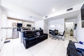 An open-concept living area features a black leather sofa, a kitchen, and a dining table — HOMESTEAD, FL