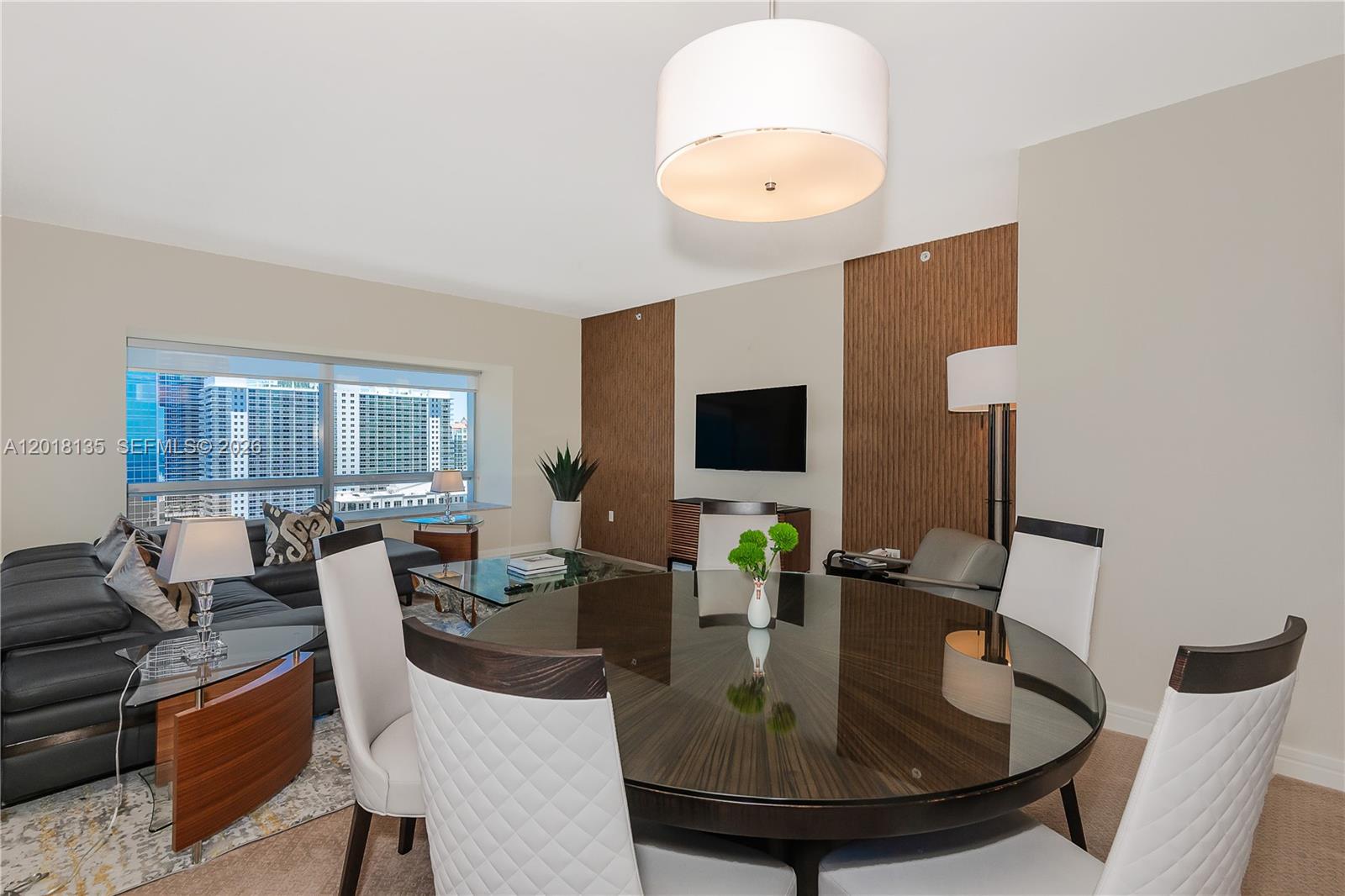 A dining area with a round glass table and white chairs sits before a living room — 1435 Brickell Ave # 3012, Miami FL 33131, MIAMI, FL