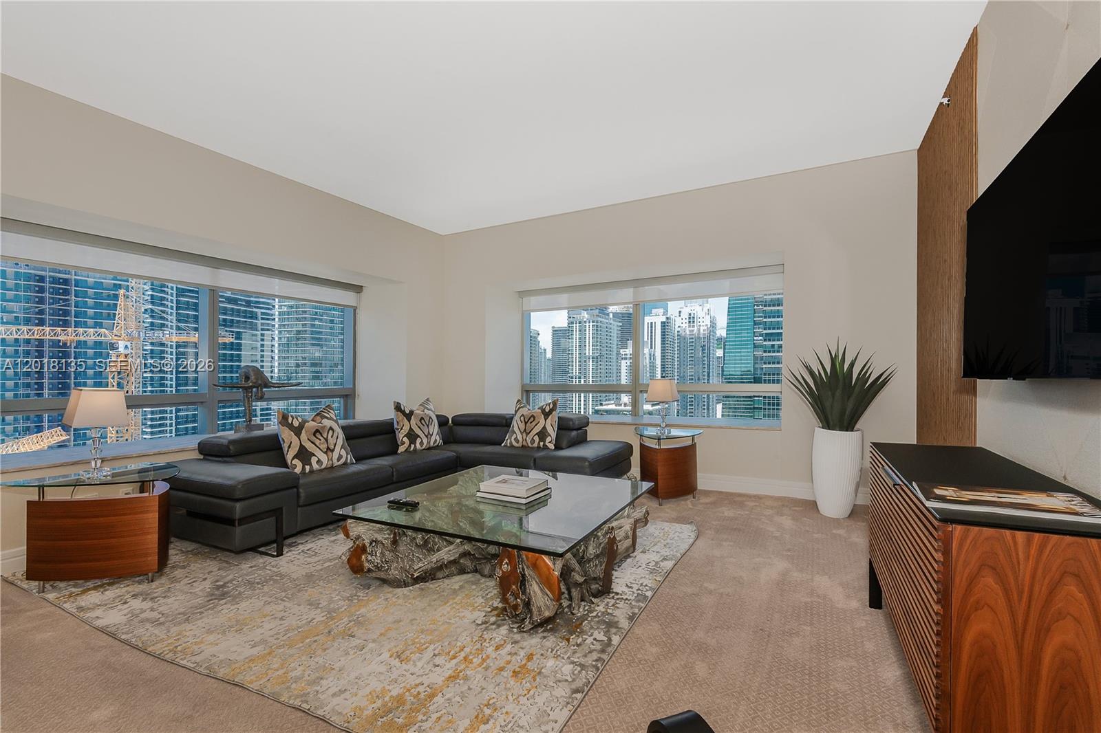 A modern living room features a sectional sofa, a glass-topped driftwood coffee table, and city views — 1435 Brickell Ave # 3012, Miami FL 33131, MIAMI, FL