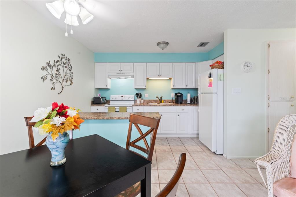 A kitchen with white cabinets, light blue walls, and a dining area in the foreground — 4351 TAHITIAN GARDENS CIRCLE UNIT C, HOLIDAY, FL