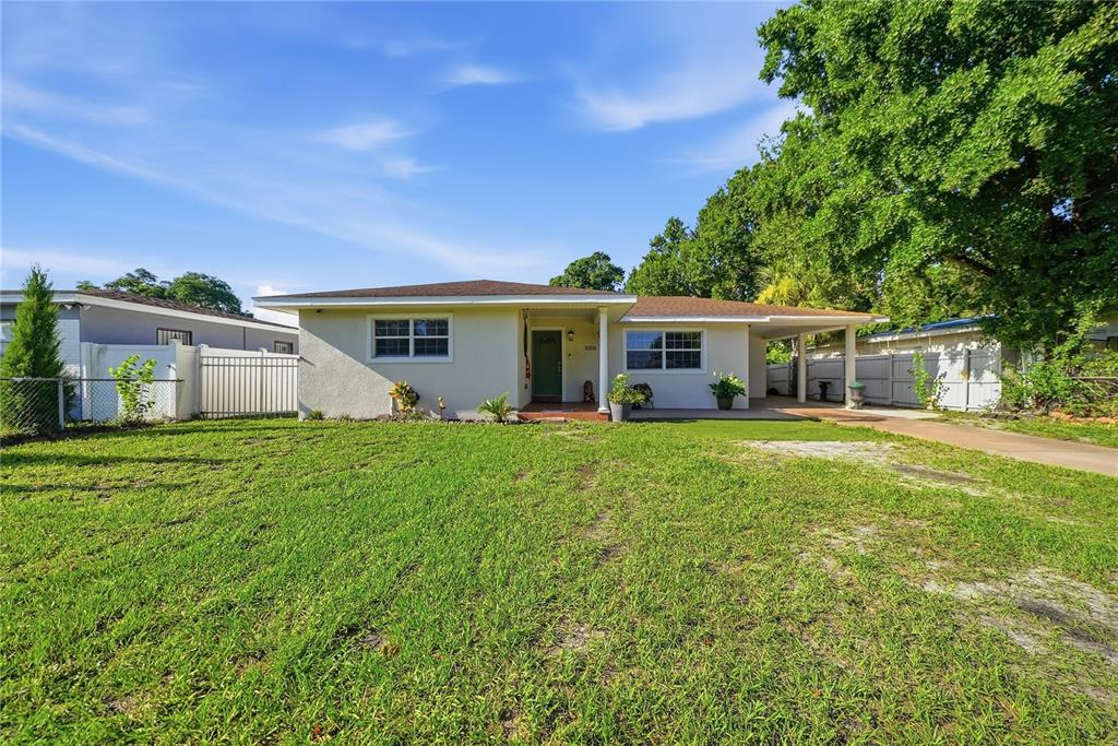 A single-story house with a light-colored exterior, a green front door, and a side carport — 3006 W SAINT CONRAD STREET, TAMPA, FL
