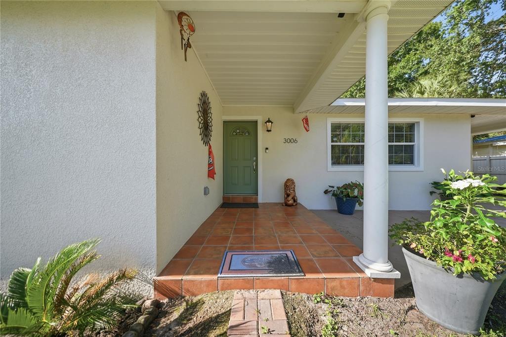 A covered front porch features tiled flooring, a green door, and a white support column — 3006 W SAINT CONRAD STREET, TAMPA, FL
