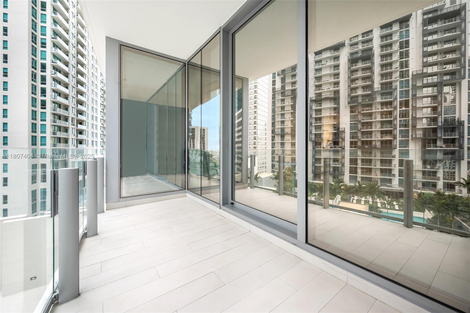 A modern balcony with white tiled flooring, glass railings, and floor-to-ceiling windows overlooking city buildings — 300 Biscayne Blvd Way # 3509, Miami FL 33131, MIAMI, FL