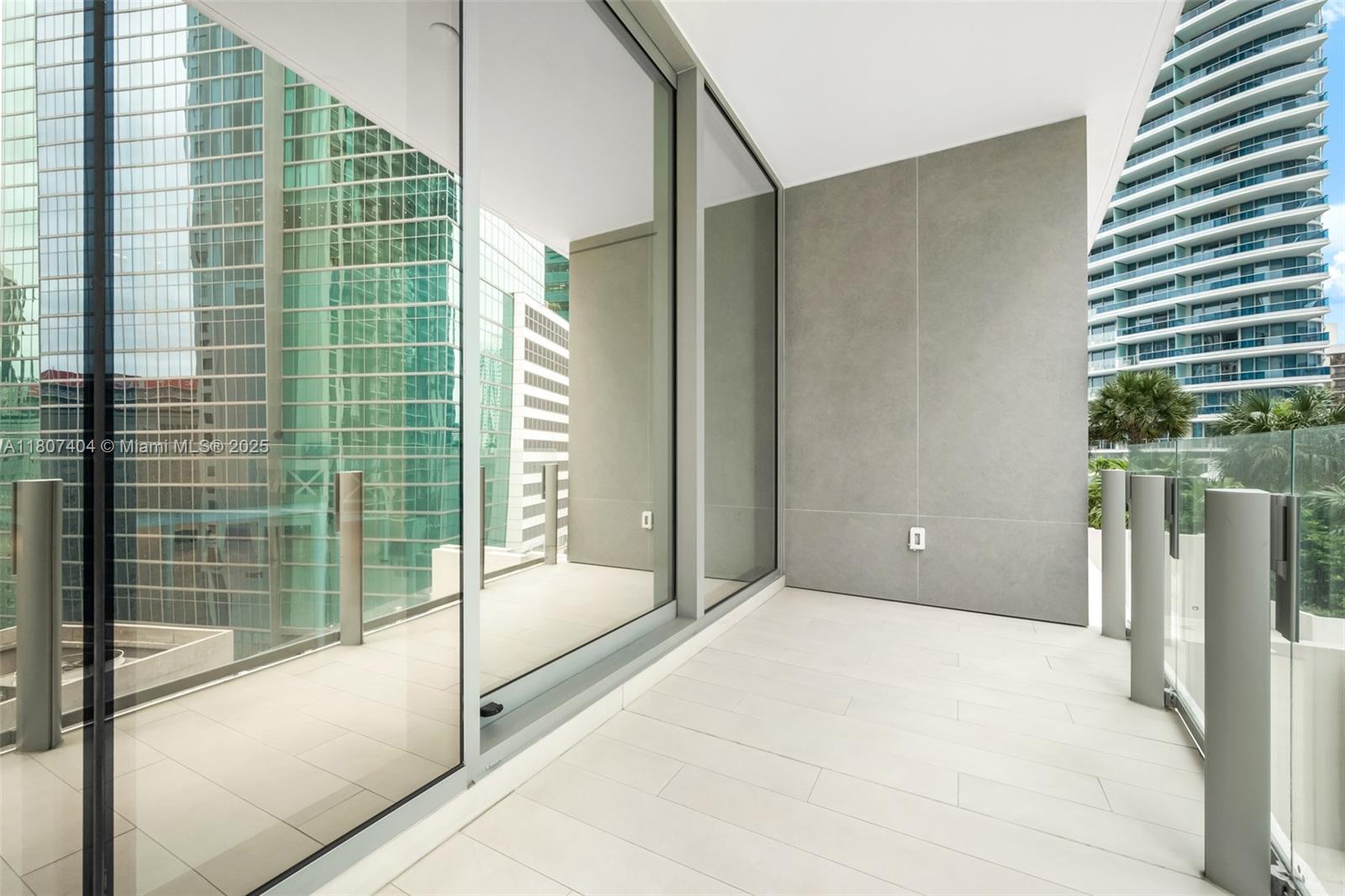 A modern balcony features large glass sliding doors, light-colored tile flooring, and a glass railing — 300 Biscayne Blvd Way # 3509, Miami FL 33131, MIAMI, FL