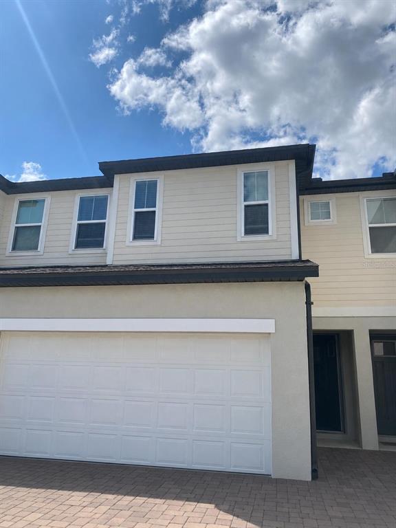 The exterior of a two-story townhouse features a garage, beige siding, and a paved driveway — 15061 WILLOW ARBOR CIRCLE, ORLANDO, FL