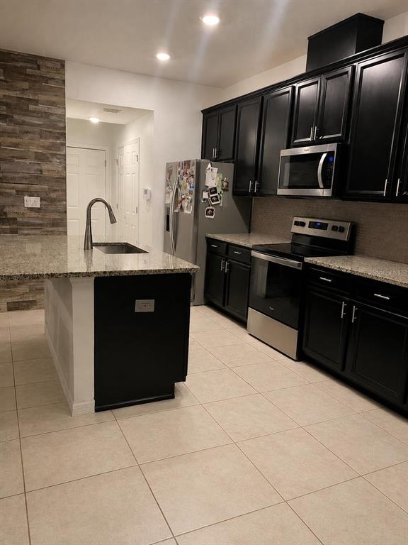 A kitchen features black cabinets, stainless steel appliances, a granite island, and tiled flooring — 15061 WILLOW ARBOR CIRCLE, ORLANDO, FL