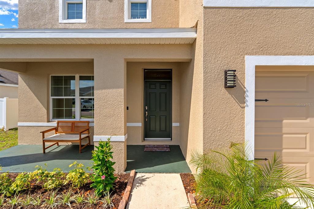 The exterior of a house features a tan stucco facade, a dark front door, and a porch — 9714 OAK RANCH CRESCENT COURT, THONOTOSASSA, FL