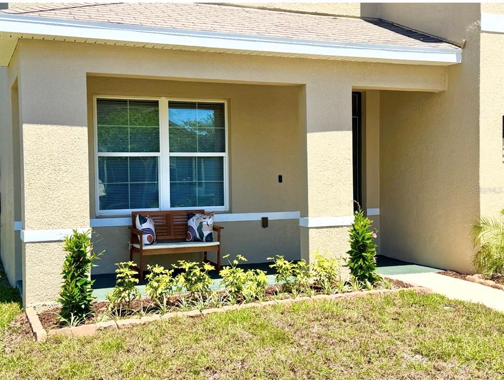 A covered front porch features a wooden bench, landscaping, and a window on a stucco home — 9714 OAK RANCH CRESCENT COURT, THONOTOSASSA, FL