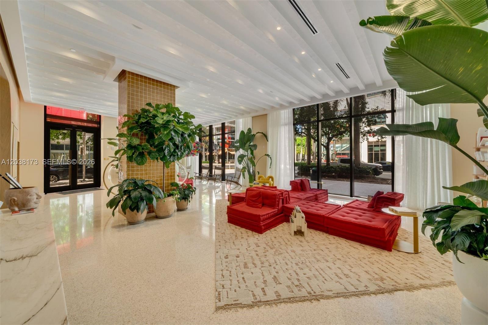 A modern lobby features a red modular sofa, large potted plants, and floor-to-ceiling windows — 90 32 # 503, Miami FL 33131, MIAMI, FL