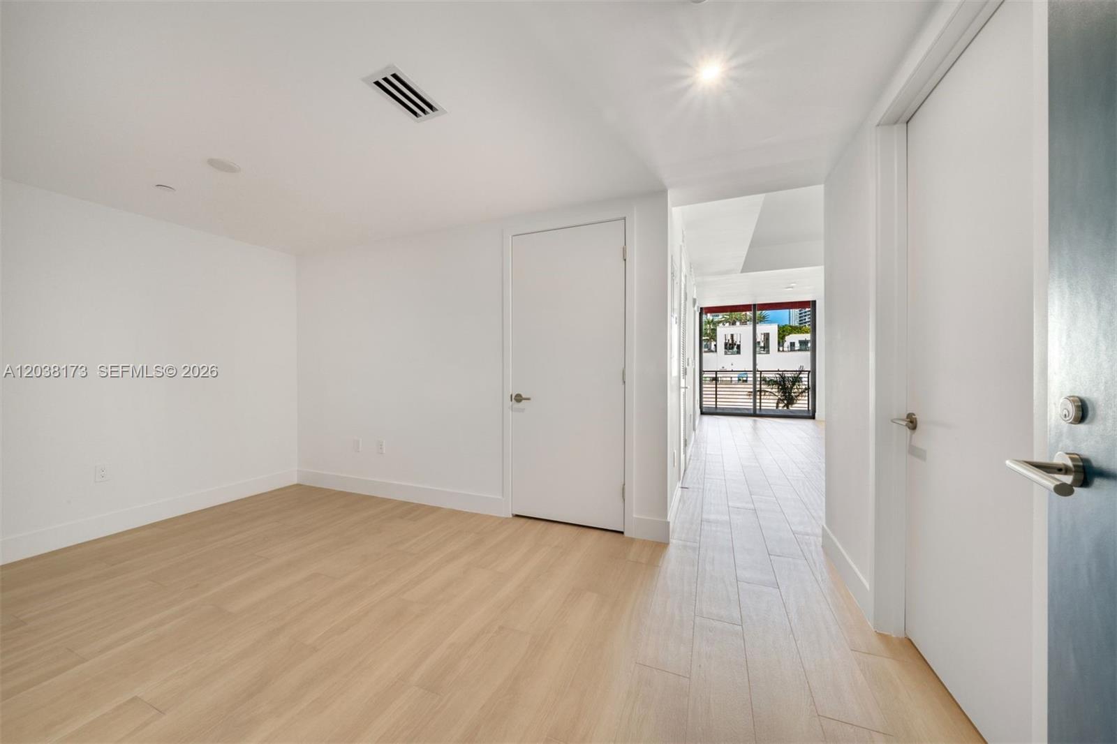 A room with light wood-look flooring leads to a hallway with a glass balcony door — 90 32 # 503, Miami FL 33131, MIAMI, FL