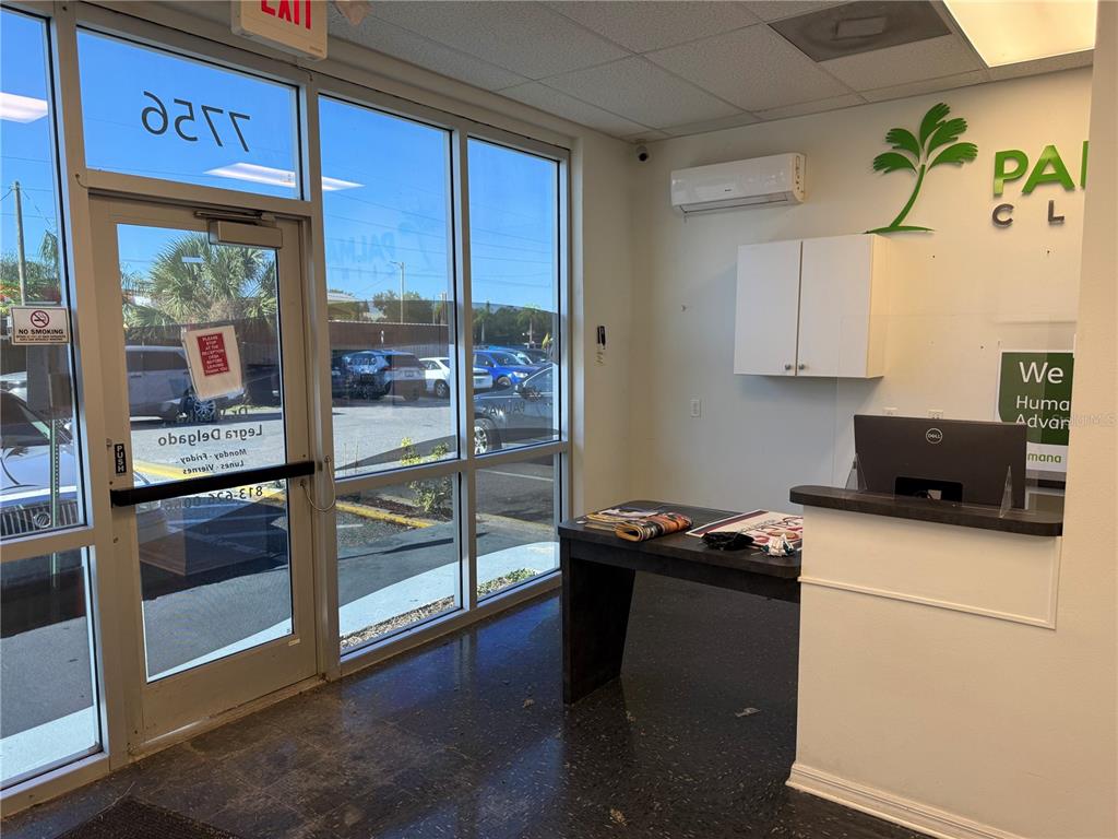A reception area features a desk, a small table, large windows, and a white wall — 7756 PALM RIVER ROAD, TAMPA, FL