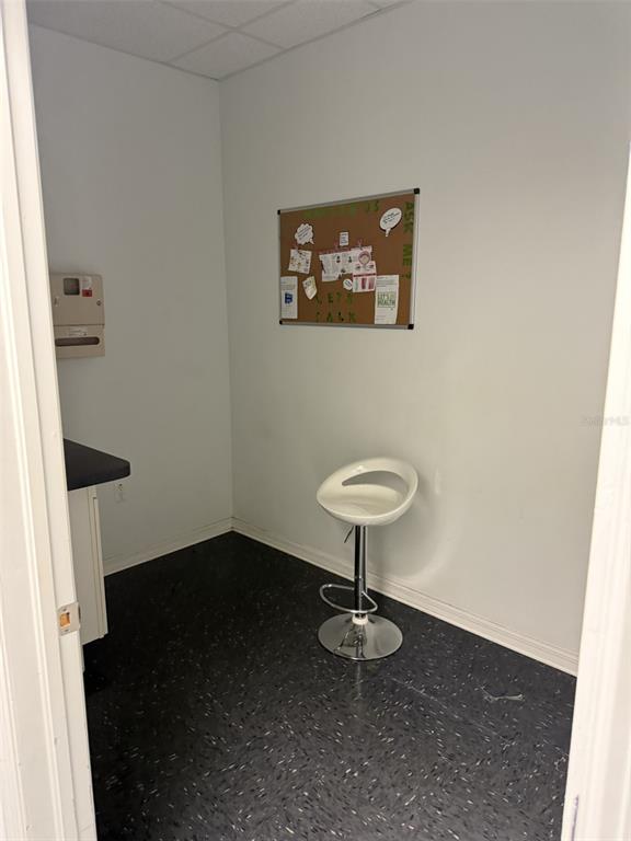 A small, sparse office room features a white bar stool, dark flooring, and a bulletin board — 7756 PALM RIVER ROAD, TAMPA, FL