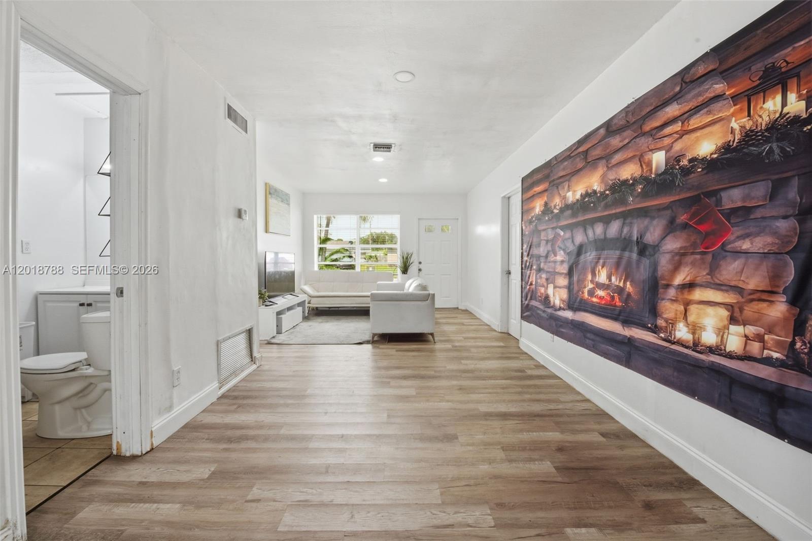 A living room with light wood-look flooring and a large fireplace tapestry on the wall — 4621 SW 31st Dr, West Park FL 33023, WEST PARK, FL
