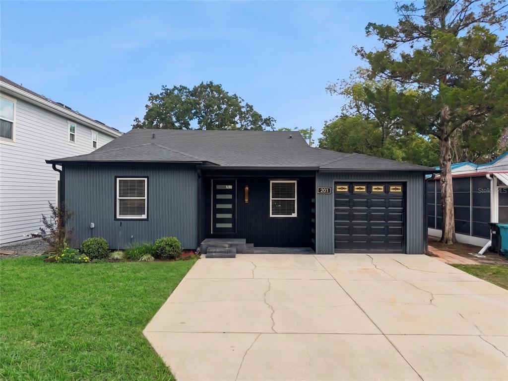 A single-story house with dark corrugated metal siding, a black garage door, and a concrete driveway — 201 E MURIEL STREET, ORLANDO, FL