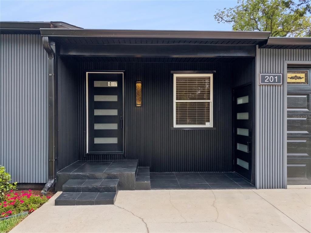 The exterior of a modern home features black vertical siding, a tiled porch, and two doors — 201 E MURIEL STREET, ORLANDO, FL