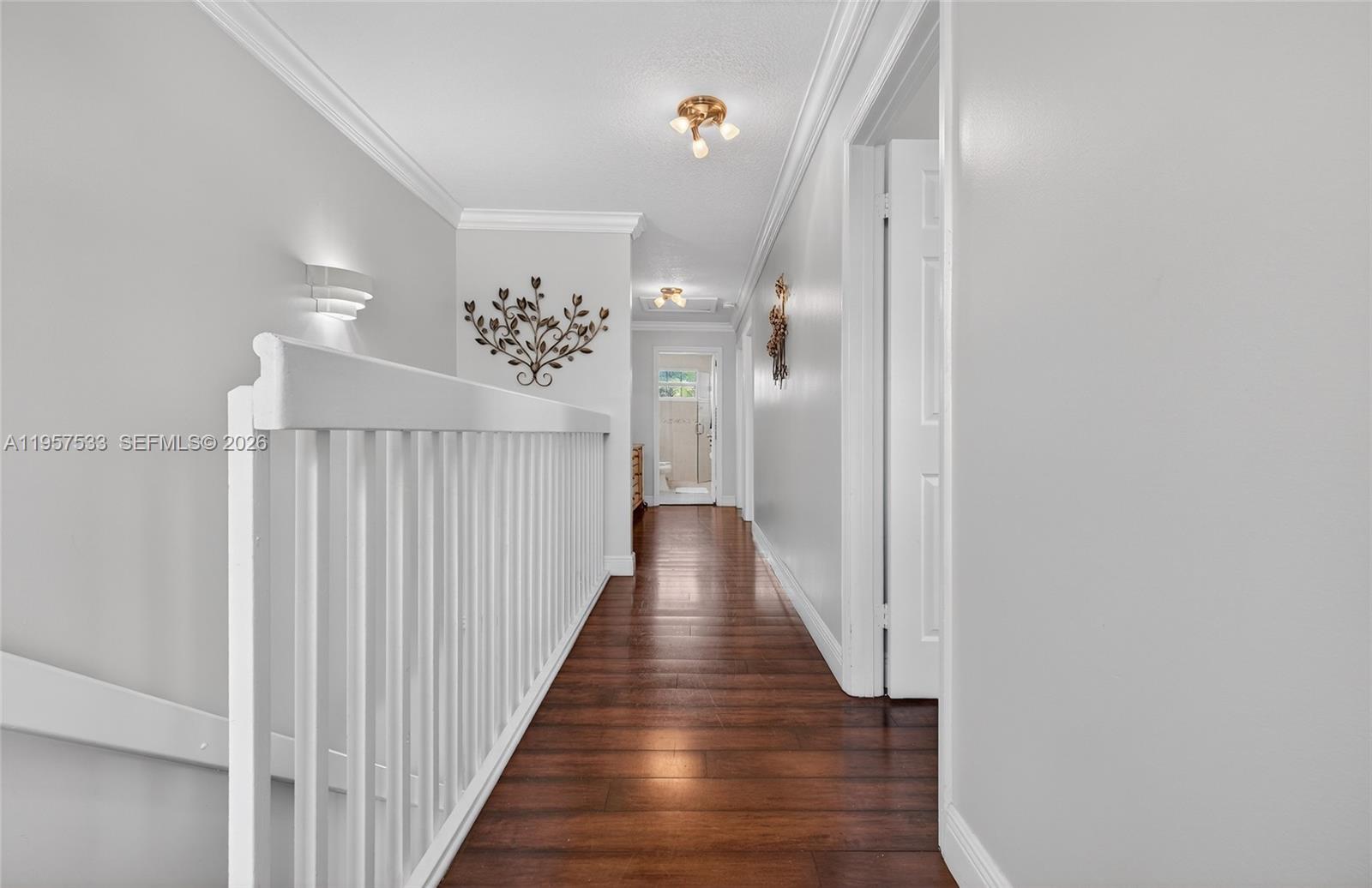 A hallway with wood flooring, white railings, and crown molding leads to a distant doorway — 1485 NW 129th Ter, Sunrise FL 33323, SUNRISE, FL