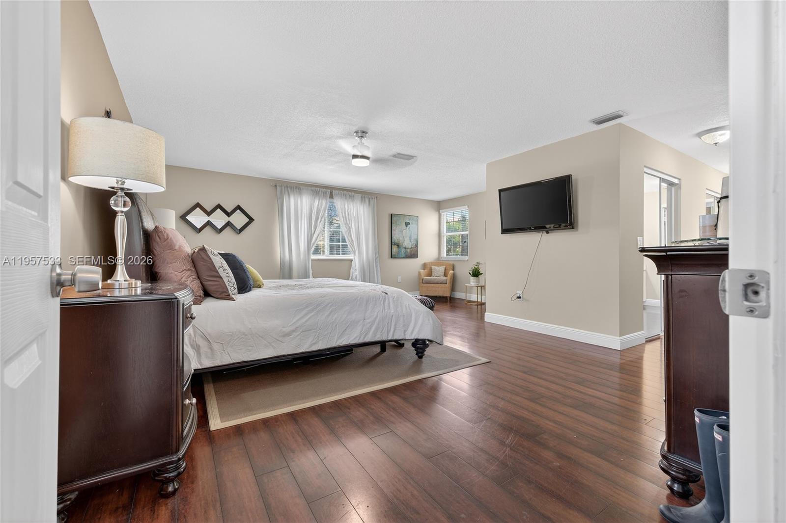 A bedroom features dark wood flooring, a bed with neutral bedding, and a wall-mounted television — 1485 NW 129th Ter, Sunrise FL 33323, SUNRISE, FL