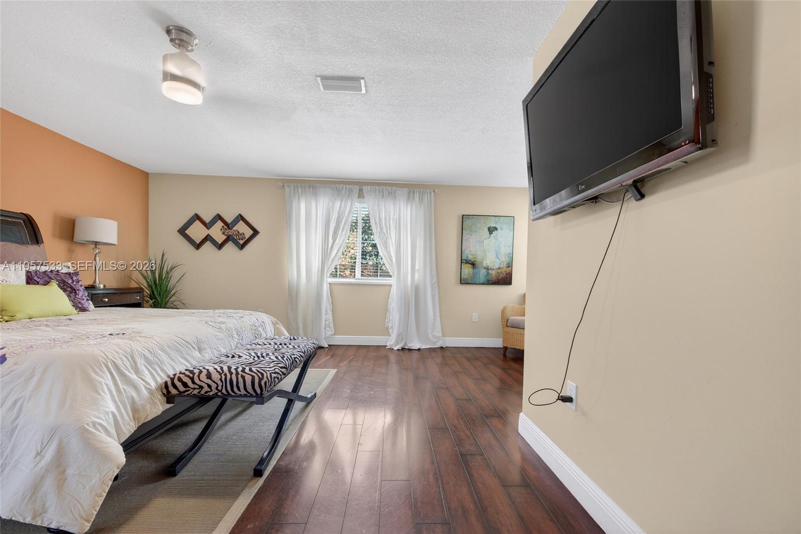 A bedroom features dark wood flooring, a zebra-print bench, and a wall-mounted television — 1485 NW 129th Ter, Sunrise FL 33323, SUNRISE, FL