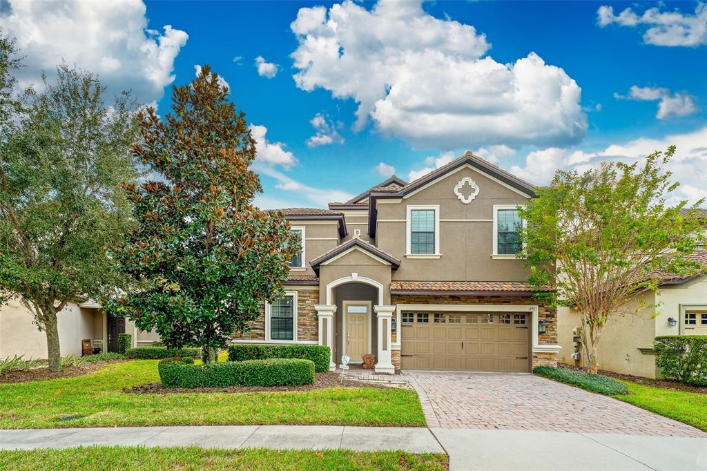 A two-story suburban house with a tan stucco exterior, stone accents, and a paved driveway — 1496 MOON VALLEY DRIVE, DAVENPORT, FL