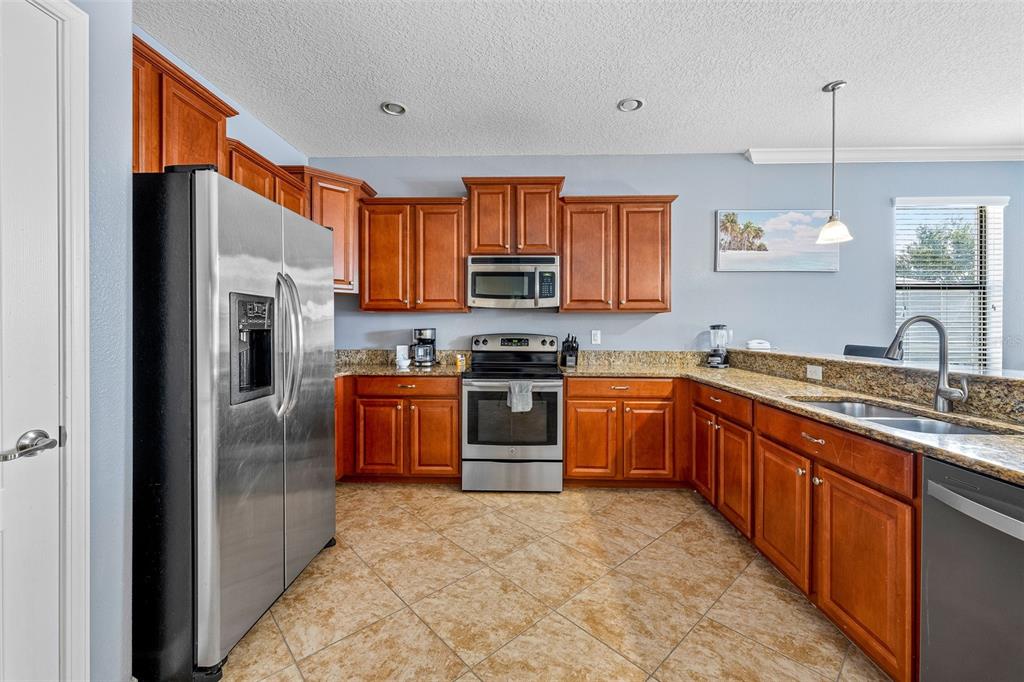 A kitchen features wood cabinets, stainless steel appliances, granite countertops, and tile flooring — 1496 MOON VALLEY DRIVE, DAVENPORT, FL
